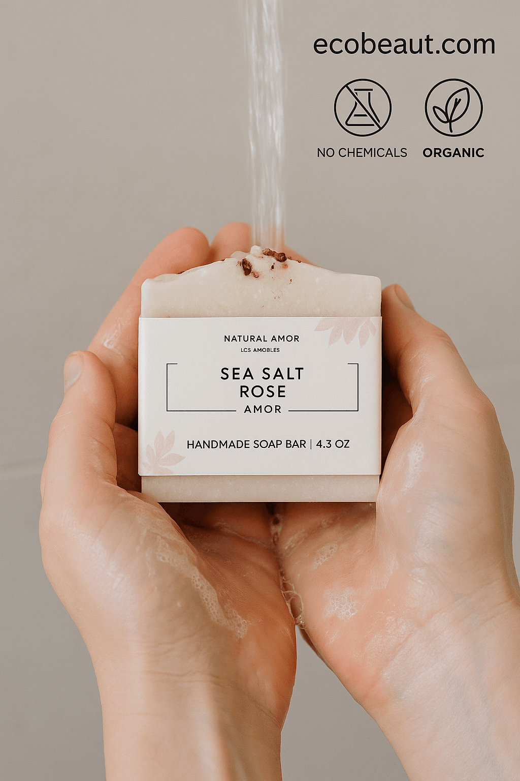 A person holds the “Sea Salt Rose Amor” handmade soap bar from ecobeaut.com under running water with soapy hands, highlighting the eco-friendly packaging and “No Chemicals” and “Organic” icons in the upper right corner.