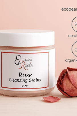 A photograph showcases a jar of rose cleansing grains by Elegant Rose, placed beside a dried rosebud on a wooden surface, with “ecobeaut.com,” “no chemicals,” and “organic products” labels elegantly displayed in the upper right corner.