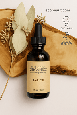 Butter Me Up Organics Hair Oil bottle on wood with beige label, next to dried leaves and ecobeaut.com branding.