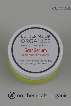 Butter Me Up Organics Scar Serum with Manuka Honey jar on a gray background, featuring ecobeaut.com in the top right and both “no chemicals” and “organic products” labels clearly shown at the bottom of the image.