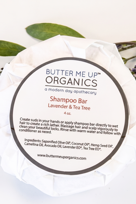 Butter Me Up Organics shampoo bar with a white background and green leaves.