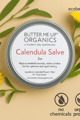 Calendula Salve in a silver tin from Butter Me Up Organics, surrounded by calendula flowers and green leaves on a beige background – ecobeaut.com, no chemicals, organic products