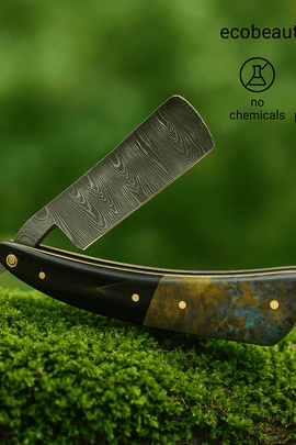 Close-up of a Damascus steel straight razor with a multicolored handle resting on lush green moss, showcasing artisanal craftsmanship with branding ecobeaut.com in the top corner.
