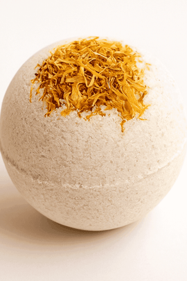 Close-up of calendula bath bomb with golden flower petals on a soft beige background, minimal and clean, ecobeaut.com