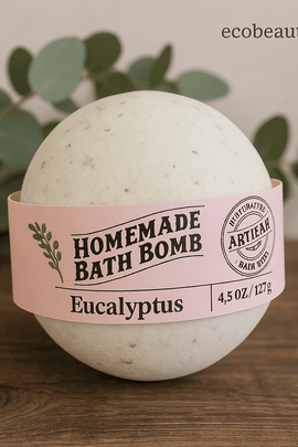 Eucalyptus handmade bath bomb with natural green specks and pink artisan label, styled on rustic wood with eucalyptus leaves in background, ecobeaut.com
