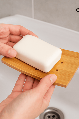 Hands placing a white soap bar on a bamboo soap dish above a sink – sustainable bathroom routine with ecobeaut.com product