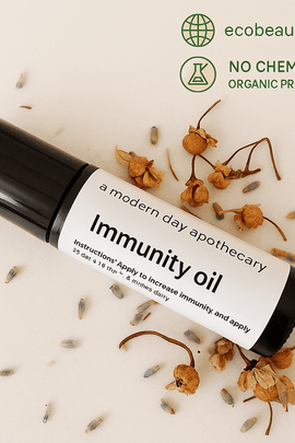 Immunity Oil bottle surrounded by dried chamomile and lavender flowers on a light surface. Organic and chemical-free product from ecobeaut.com.