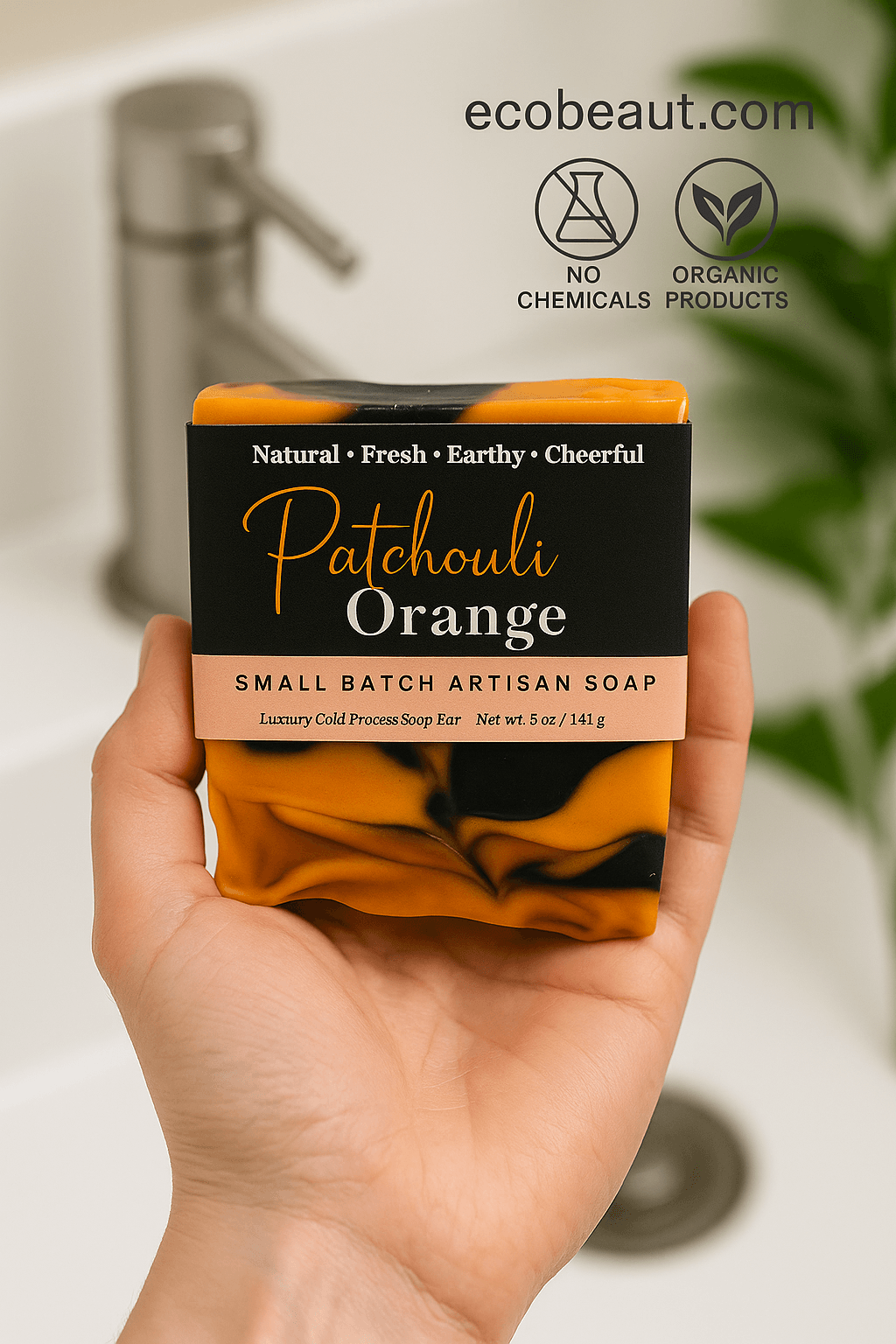 Light-skinned hand using Patchouli Orange artisan soap from ecobeaut.com, with “NO CHEMICALS” and “ORGANIC PRODUCTS” icons in the top right corner.