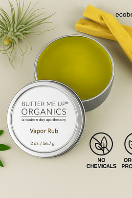 "Open tin of Butter Me Up Organics Vapor Rub with green balm, surrounded by palo santo sticks and leaves, eco labels, and ecobeaut.com branding in the top right corner."