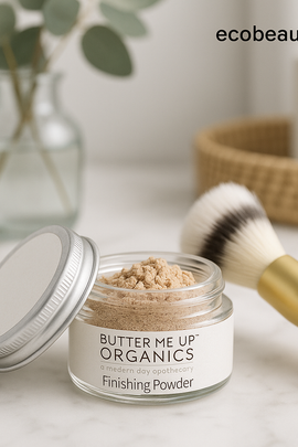 Jar of Butter Me Up Organics Finishing Powder with a brush on a light surface, featuring ecobeaut.com branding.