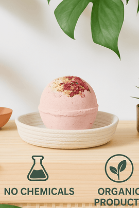 Organic pink bath bomb with dried rose petals and chamomile, styled in a white rope dish on a wooden shelf with lush green plants — eco-friendly decor, ecobeaut.com