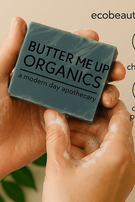 Person holding a lathered 'Butter Me Up Organics' soap bar while washing hands, with green leaves in the background, and eco labels 'no chemicals', 'organic products', and website ecobeaut.com displayed in the upper right corner.