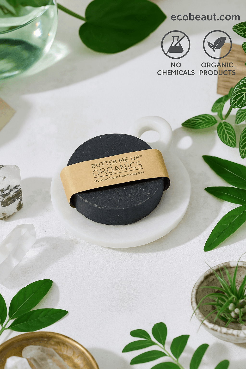 Round black organic soap bar from ecobeaut.com on a marble dish, surrounded by green leaves and crystals, with “NO CHEMICALS” and “ORGANIC PRODUCTS” icons in the top right corner.