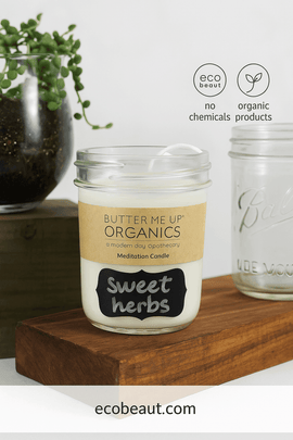 Soy wax essential oil candle with 'Sweet Herbs' label, displayed on a wooden block next to a glass jar and greenery – ecobeaut.com – no chemicals, organic products