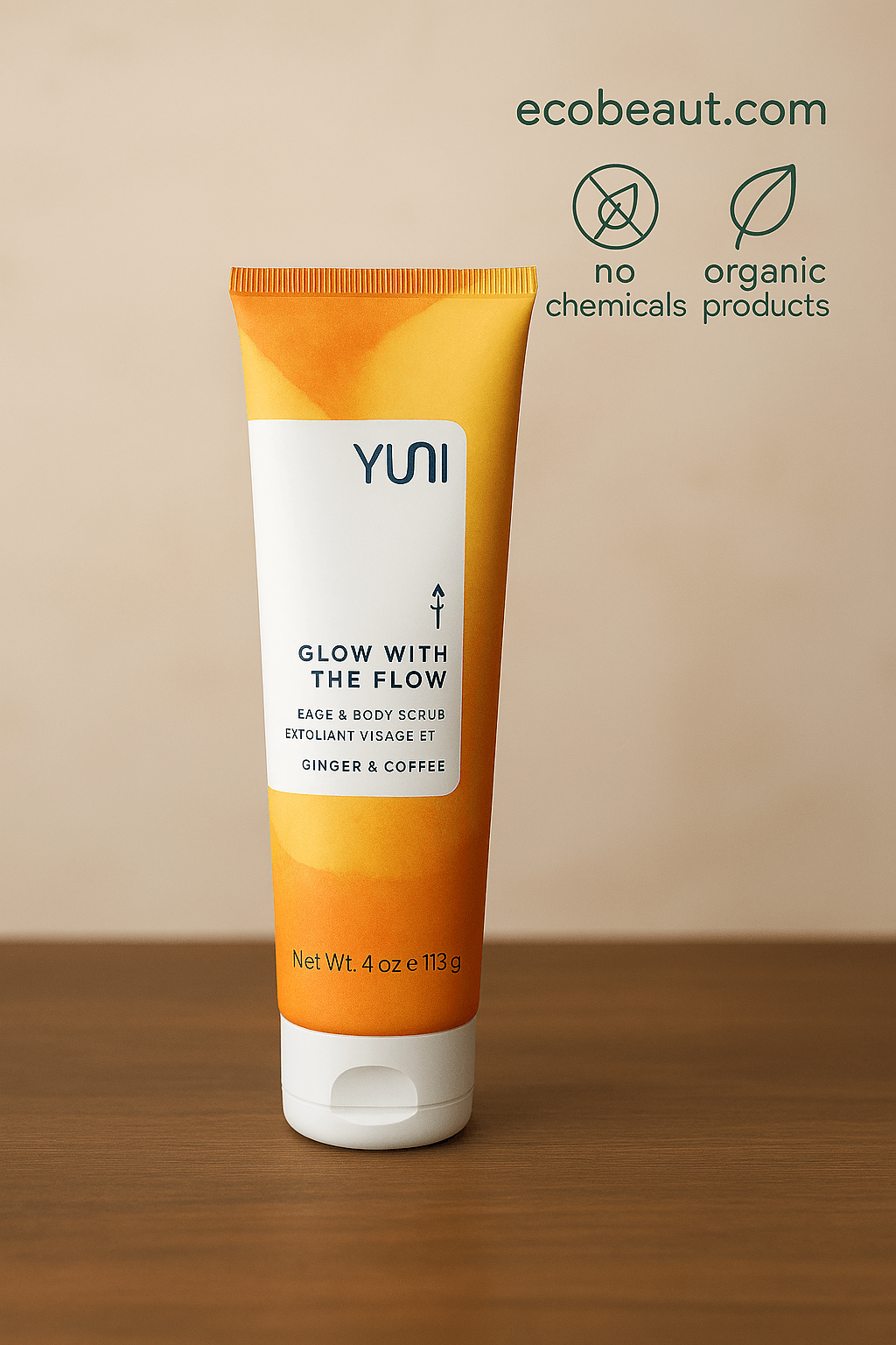 YUNI Glow With The Flow Face & Body Scrub in a vibrant orange-yellow tube, displayed close-up against a soft beige background, with eco-friendly icons and ecobeaut.com URL in the top right corner
