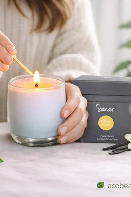 Person lighting a candle with 'Sanari' packaging in the background, featuring 'ecobeaut.com'.