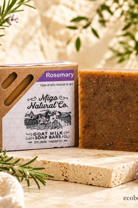 A bar of Migo Natural Co. Rosemary goat milk soap stands next to its kraft paper box packaging.