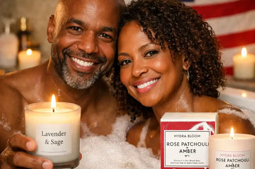 African American couple relaxing in a bubble bath holding natural scented candles, featuring Ecobeaut.com Hydra Bloom Rose Patchouli Amber candle with American flag background
