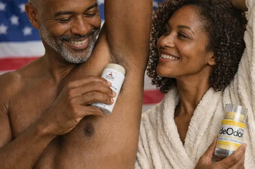Black couple using natural deodorants in a bathroom, man applying Shave Essentials Eucalyptus & Mint and woman holding deOdor Lemongrass Bergamot, with American flag background and ecobeaut.com logo.