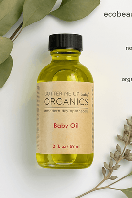 A Butter Me Up Organics Baby Oil bottle sits on a white background with green leaves and buds around it. Eco-labels and the website ecobeaut.com appear in the top right.