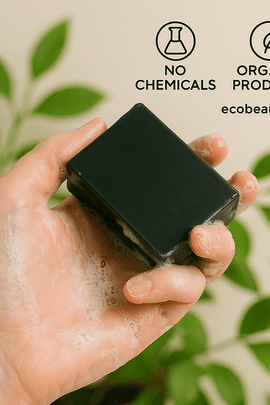  A fair-skinned hand lathers a black soap bar from ecobeaut.com, surrounded by green leaves, with “NO CHEMICALS” and “ORGANIC PRODUCTS” icons in the upper right corner.