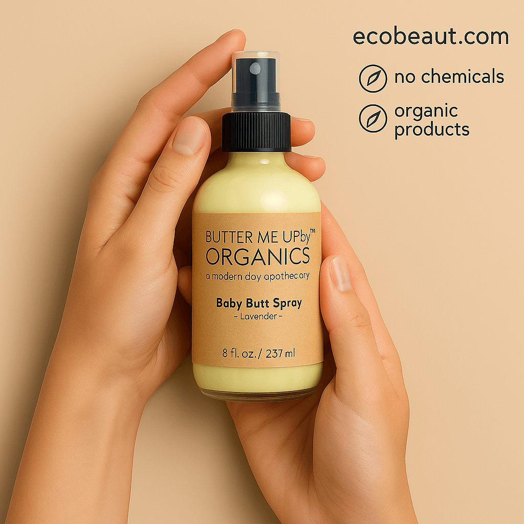 A pair of hands holds a Butter Me Up Organics Baby Butt Spray bottle with a kraft label, while the top right corner displays ecobeaut.com and eco-friendly icons for no chemicals and organic products.





