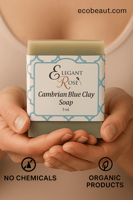 A person gently holds a Cambrian Blue Clay Soap bar from Elegant Rose with both hands. 'ecobeaut.com' appears in the top right corner, and eco icons 'NO CHEMICALS' and 'ORGANIC PRODUCTS' are shown at the bottom.