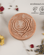 A round artisan soap with a lotus design sits on a marble surface, surrounded by dried flowers and petals, with eco-friendly icons “No Chemicals” and “Organic Products” and ecobeaut.com displayed in the upper right corner.




