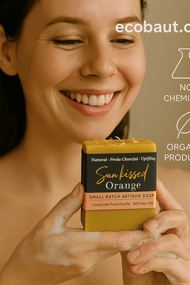 A smiling woman holds a Sun kissed Orange soap bar from ecobeaut.com with lather on her hands, featuring “NO CHEMICALS” and “ORGANIC PRODUCTS” icons in the upper right corner.