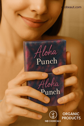 A smiling woman holds two Aloha Punch soap bars from ecobeaut.com, with 'NO CHEMICALS' and 'ORGANIC PRODUCTS' labels displayed below the image on a neutral background