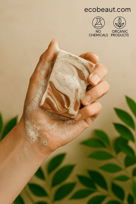 A woman’s hand lathers Vanilla Tangerine soap from ecobeaut.com with foam and green leaves in the background, featuring “NO CHEMICALS” and “ORGANIC PRODUCTS” icons in the upper right corner.