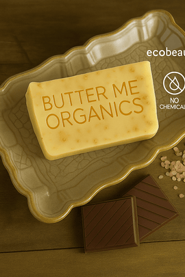 Butter Me Organics soap bar on ceramic dish with pink salt and chocolate squares, featuring “NO CHEMICALS,” “ORGANIC PRODUCTS” icons, and ecobeaut.com branding in the top right corner.



