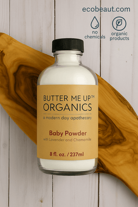 Butter Me Up Organics Baby Powder bottle placed on a wood slab with eucalyptus leaves, eco-labels, and ecobeaut.com displayed in the top right corner.