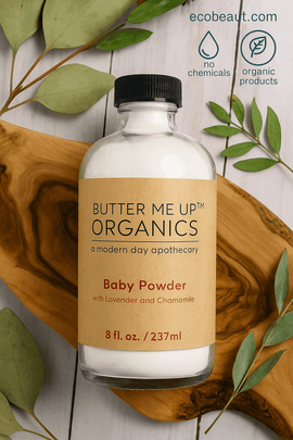 Butter Me Up Organics Baby Powder bottle placed on a wood slab with eucalyptus leaves, eco-labels, and ecobeaut.com displayed in the top right corner.





