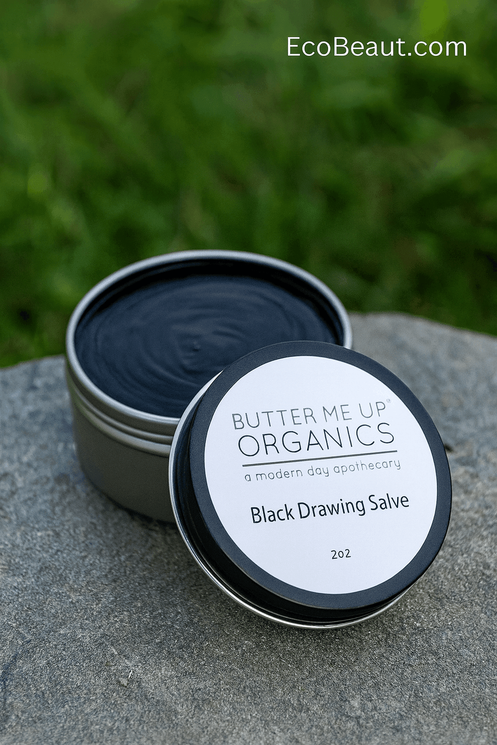 Butter Me Up Organics Black Drawing Salve tin on natural stone with green nature background, eco-friendly organic healing balm, EcoBeaut.com branding