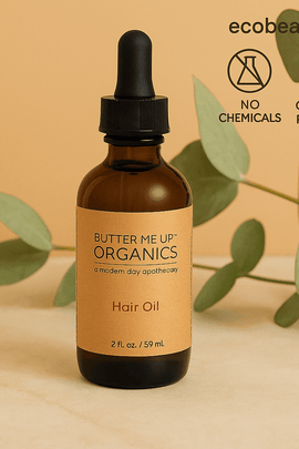 Butter Me Up Organics Hair Oil bottle on marble surface with eucalyptus leaves, ecobeaut.com, and organic icons above.





