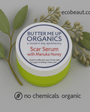 Butter Me Up Organics Scar Serum with Manuka Honey jar on a gray background, featuring ecobeaut.com in the top right and both “no chemicals” and “organic products” labels clearly shown at the bottom of the image.