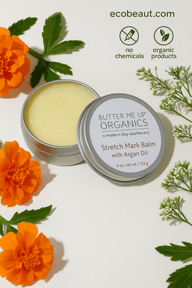 Butter Me Up Organics Stretch Mark Balm in a silver tin with the lid slightly open, surrounded by marigold and white flowers on a textured off-white surface, featuring no chemicals and organic products icons with ecobeaut.com in the top right corner








