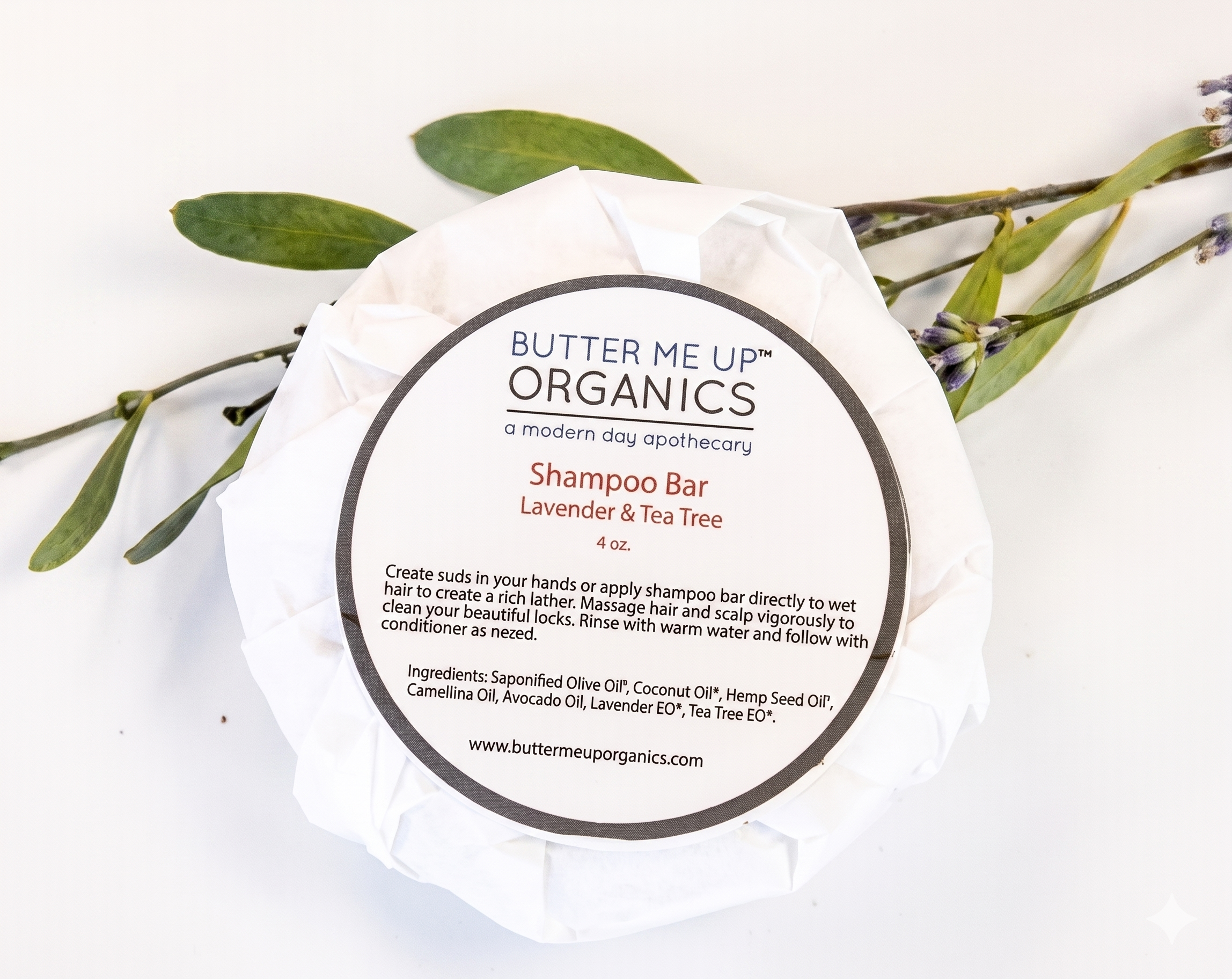 Butter Me Up Organics shampoo bar with a white background and green leaves.