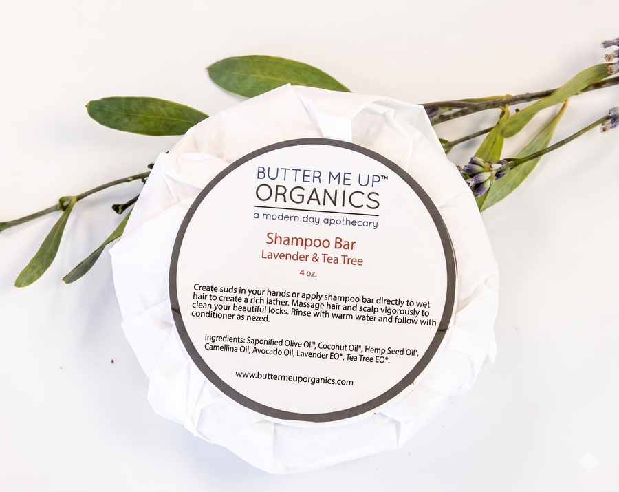 Butter Me Up Organics shampoo bar with a white background and green leaves.