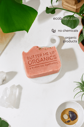 Close-up of Butter Me Up Organics pink soap bar with embossed label and herbal topping, featuring ecobeaut.com, no chemicals and organic products – handmade natural soap USA