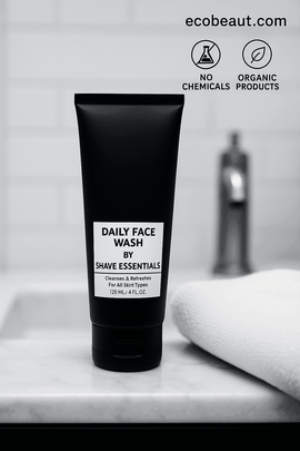 Close-up of Daily Face Wash by Shave Essentials standing on a clean marble counter with a white towel and blurred faucet in the background, labeled with ecobeaut.com and 'no chemicals, organic products' icons.
