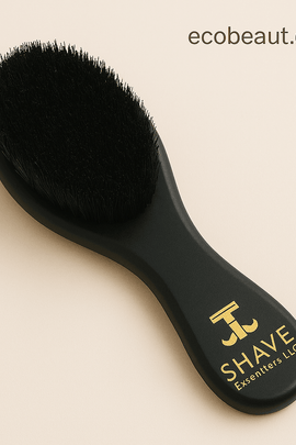 Close-up of premium black boar bristle beard brush by SHAVE Essentials LLC with gold logo, shown on a soft neutral background — ecobeaut.com