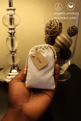 Dark-skinned hand holding natural muslin bath tea bag – labeled “Soap,” eco-friendly and handmade herbal soak for relaxation