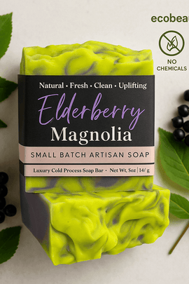 Elderberry Magnolia artisan soap bar with green and purple swirls, surrounded by elderberry leaves and berries, labeled with no chemicals and organic product icons, ecobeaut.com in the top right corner.