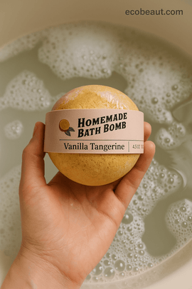 Hand holding a Vanilla Tangerine bath bomb from ecobeaut.com over a foamy bath – fizzy moisturizing soak for home spa rituals