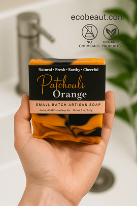Light-skinned hand using Patchouli Orange artisan soap from ecobeaut.com, with “NO CHEMICALS” and “ORGANIC PRODUCTS” icons in the top right corner.







