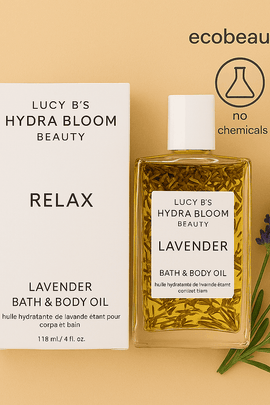 Lucy B’s Hydra Bloom Lavender Bath & Body Oil with product box, surrounded by fresh lavender sprigs. Top right corner displays ecobeaut.com and icons: no chemicals, organic products.