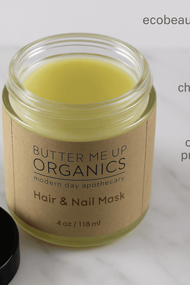 Open jar of Butter Me Up Organics Hair & Nail Mask placed on a white marble surface, with the label clearly visible. In the top right corner, the website "ecobeaut.com" is displayed alongside icons reading "no chemicals" and "organic products."
