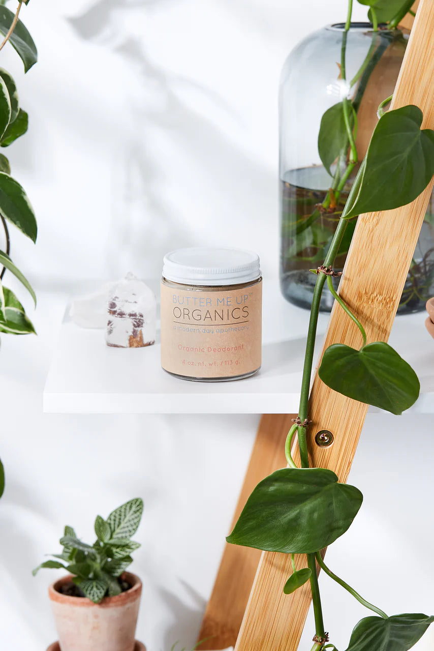 Jar of 'Nourish Organics' on a white surface with plants in the background